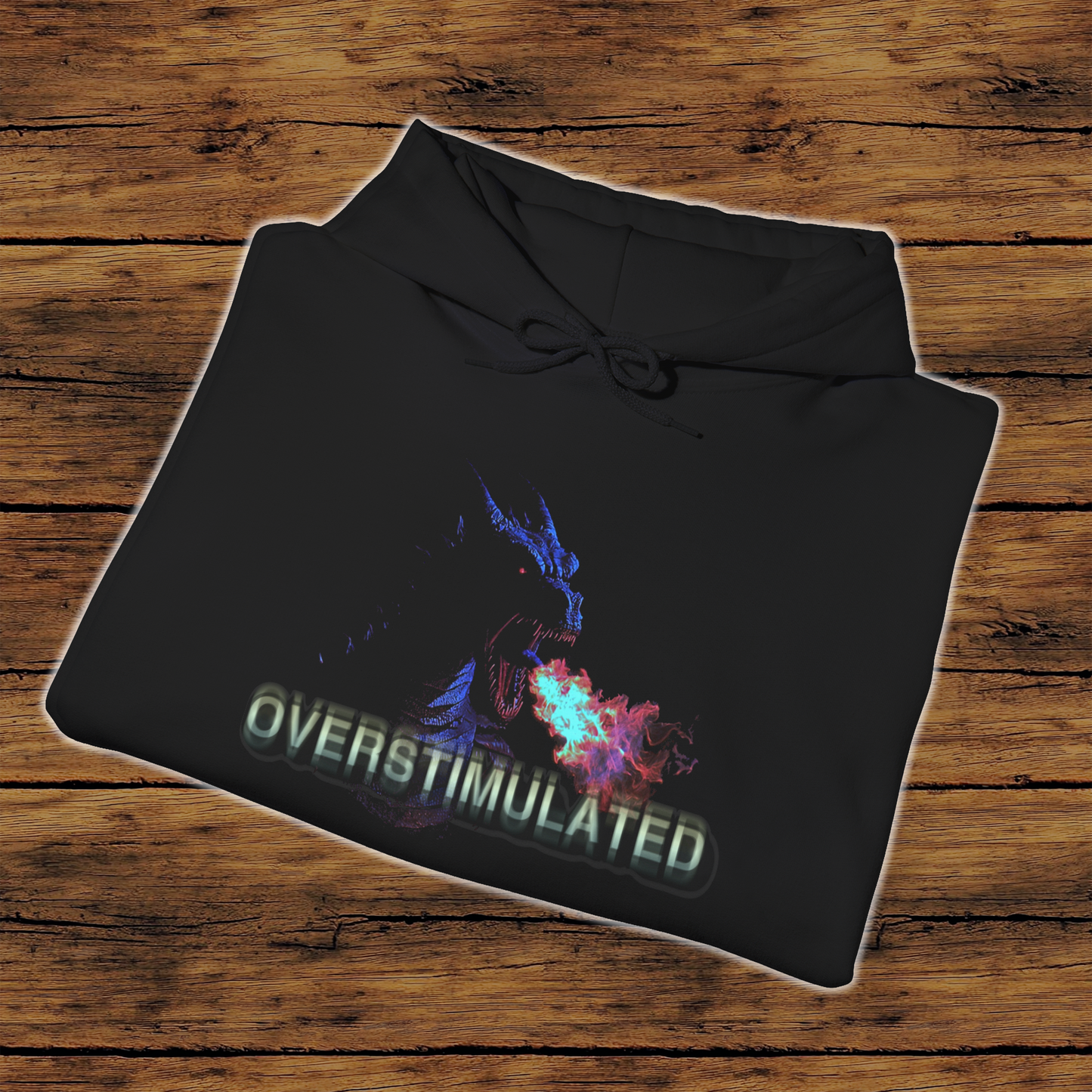 A black hooded sweatshirt folded with the text 'OVERSTIMULATED' printed on the front, featuring a graphic of a dragon breathing fire.